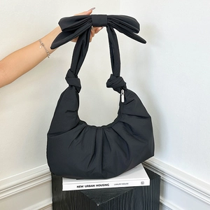 Minimalist black pleated half-moon shoulder bag featuring a large bow and silver zipper