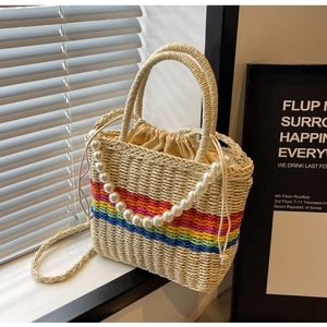 Detail of woven straw handbag featuring rainbow stripes and faux pearl shoulder strap