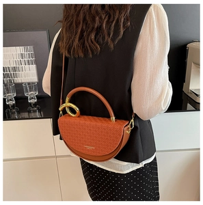 Detailed view of brown textured saddle bag with gold metal ring and cross-weave pattern