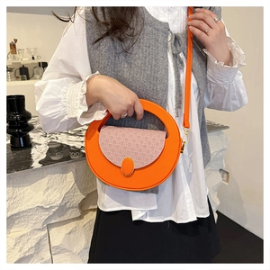 Detail of round orange crossbody bag with woven pink flap shown on a model