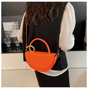 Detail of orange saddle bag with woven texture and gold ring hardware on a model