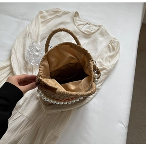 Close-up of woven straw bag detail featuring large white pearls and satin drawstring lining