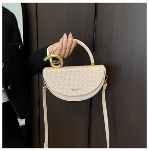 Detail of beige saddle bag showing woven texture and gold twisted ring on handle