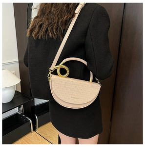 Detail of beige quilted saddle bag with gold metal handle on a model in a dark interior