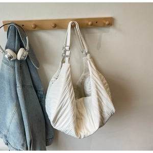 Detail of white pleated hobo bag texture and silver metal hardware on a wooden rack