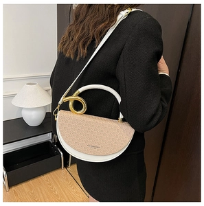 Detail of a two-tone saddle bag with woven khaki flap and gold ring handle worn by model