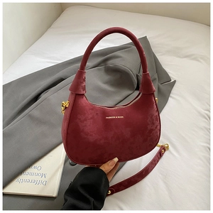 Macro shot of burgundy velvet crescent bag with gold logo and wide shoulder strap