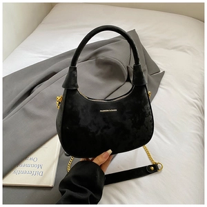 Close-up of black velvet crescent bag with gold chain strap and elegant brand lettering