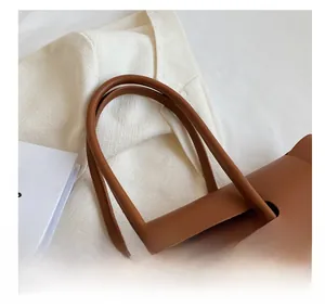 Detail of rounded leather handles with neat stitching on a brown tote bag