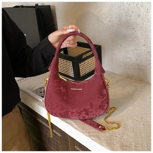 Close-up of deep red velvet crescent bag with gold chain strap and brand lettering
