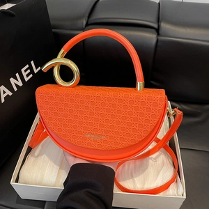 Bright orange saddle bag with woven texture and gold metal handle in a white gift box