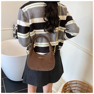 Brown velvet crescent bag shown as a shoulder bag on a model with a gold chain strap