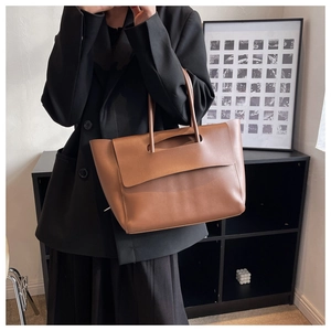 Detail of a brown leather tote bag showing a trapezoidal structure and smooth matte texture