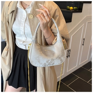 Detailed view of grey velvet crescent bag with gold chain and branded logo texture