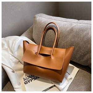 Detail of caramel leather tote bag resting on a white suit jacket in a cozy setting