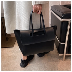 Minimalist black leather tote bag with unique top cutout and round handle detail