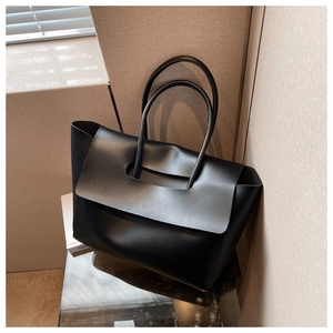 Detail of black matte leather tote bag with unique flap handle design in indoor setting