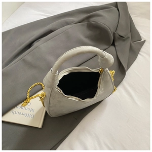 Detail of light gray velvet crescent bag with gold chain strap on a blazer