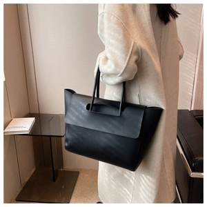 Detail view of large black leather tote bag with flap closure on cream coat