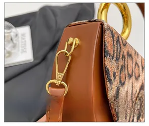 Detailed close-up of leopard print flap and golden metal clasp on a brown handbag