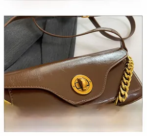 Close-up of vintage gold twist lock and glossy brown leather texture on a mini bag