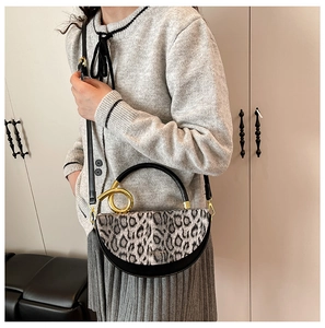 Detail of a chic half-moon handbag featuring leopard print texture and a gold ring handle