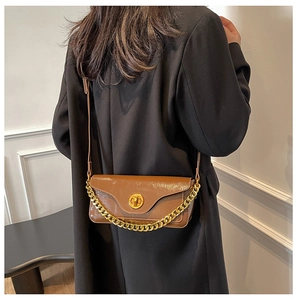 Brown faux leather crossbody bag with golden chain and clasp worn over black coat