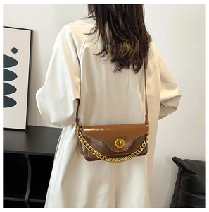 Close-up of brown glossy leather bag with gold chain and round metal turn-lock