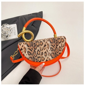 Detail view of orange handbag with leopard print flap and spiral gold metal handle