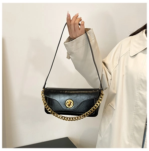 Detail of black glossy leather shoulder bag with bold gold chain and circular twist lock