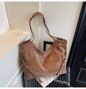 Détail du sac cabas en similicuir marron texturé avec anneaux métalliques sur une valise