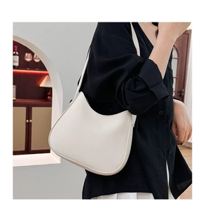 Close-up of minimalist white half-moon shoulder bag showing smooth texture and wide strap