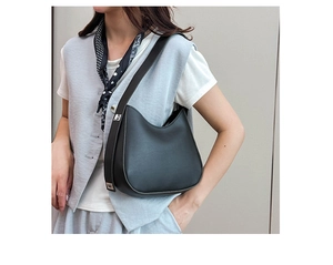 Minimalist black leather crescent bag worn by a model against a neutral interior wall