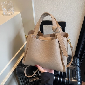 Borsa a secchiello beige con trama litchi e dettagli dorati su una valigia nera