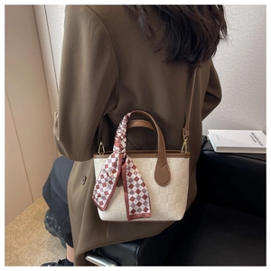 Detail of cream woven handbag with brown leather trim and plaid silk scarf on the handle
