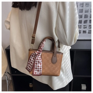 Close-up of a brown checkered texture handbag with a decorative plaid scarf on handle