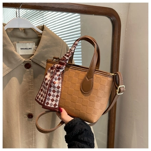Detail of brown textured handbag with plaid scarf handle and gold hardware zipper