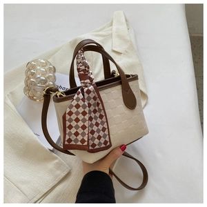 Detail of elegant cream textured handbag with brown leather handle and plaid silk scarf decoration