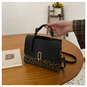 Detail view of leopard print crossbody bag with black leather flap and golden oval buckle
