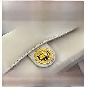Détail d'un fermoir rotatif doré sur un sac à main minimaliste en cuir blanc cassé