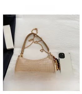 Detail view of beige crocodile embossed baguette bag with chain strap and beaded charm