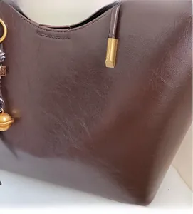 Close-up of brown leather tote bag with soft texture, metal bell and oil-wax finish