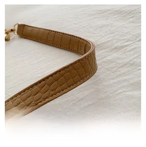 Detail of crocodile embossed leather strap with gold lobster clasp on brown bag