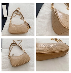 Detail view of beige crocodile embossed baguette bag with metal chain and wooden bead tassel