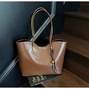 Detailed view of brown tote bag featuring glossy leather texture and golden bell pendant