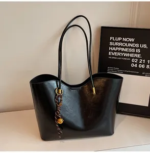 Detail of black leather tote bag with braided rope charm and golden ball accessory