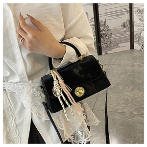Détail du sac à main noir brillant avec fermoir doré rotatif et pendentif tressé
