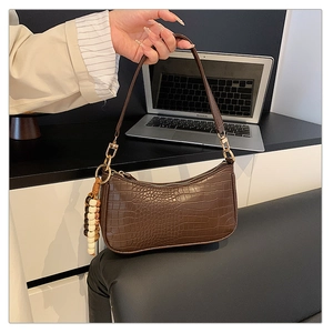 Detail of dark brown faux crocodile baguette bag with distinctive beaded tassel charm