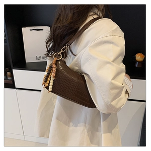 Close-up of brown crocodile texture handbag with decorative beaded tassel accessory