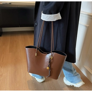 Detail of a large brown oil-wax tote bag with vintage metal charm and slim shoulder straps